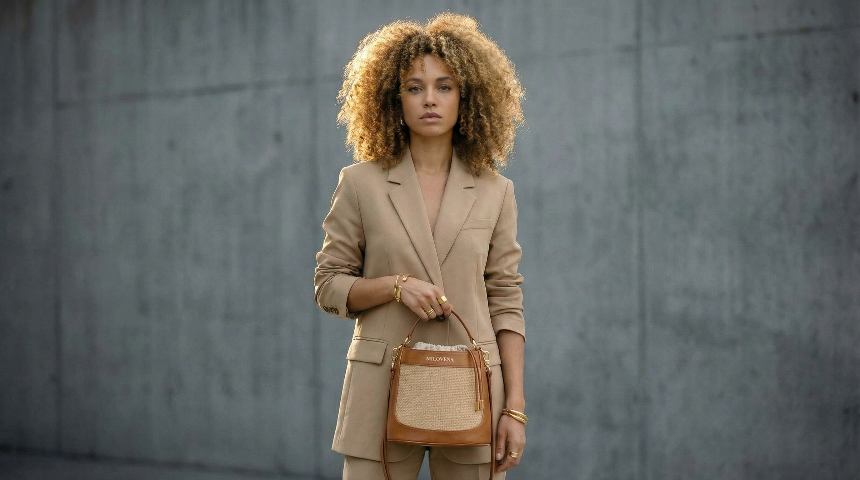 Confident woman standing in an urban concrete setting wearing the Milovena Vertical bag in cognac